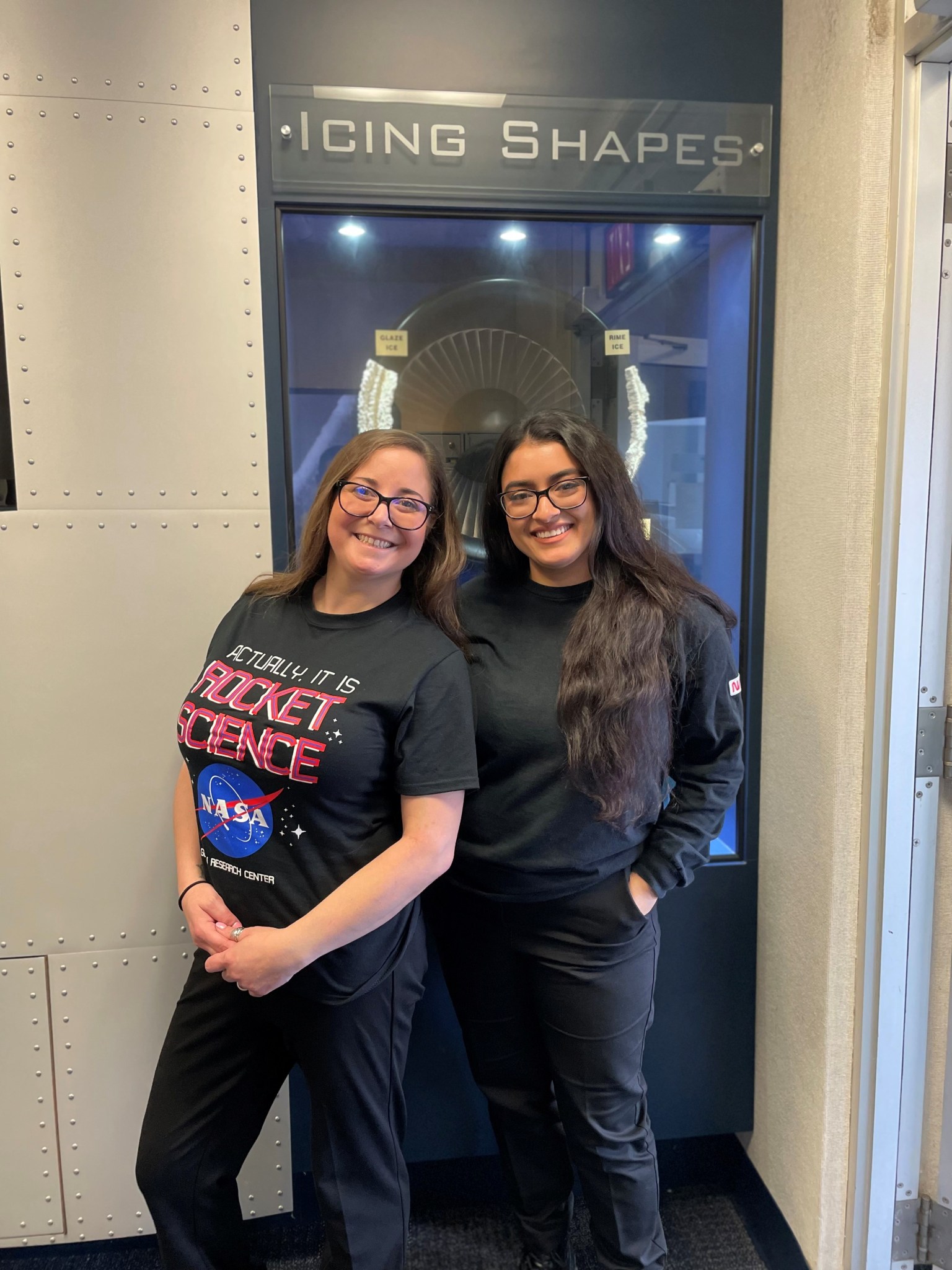 Two interns standing in front of a lab window with the words Icing Shapes above the window