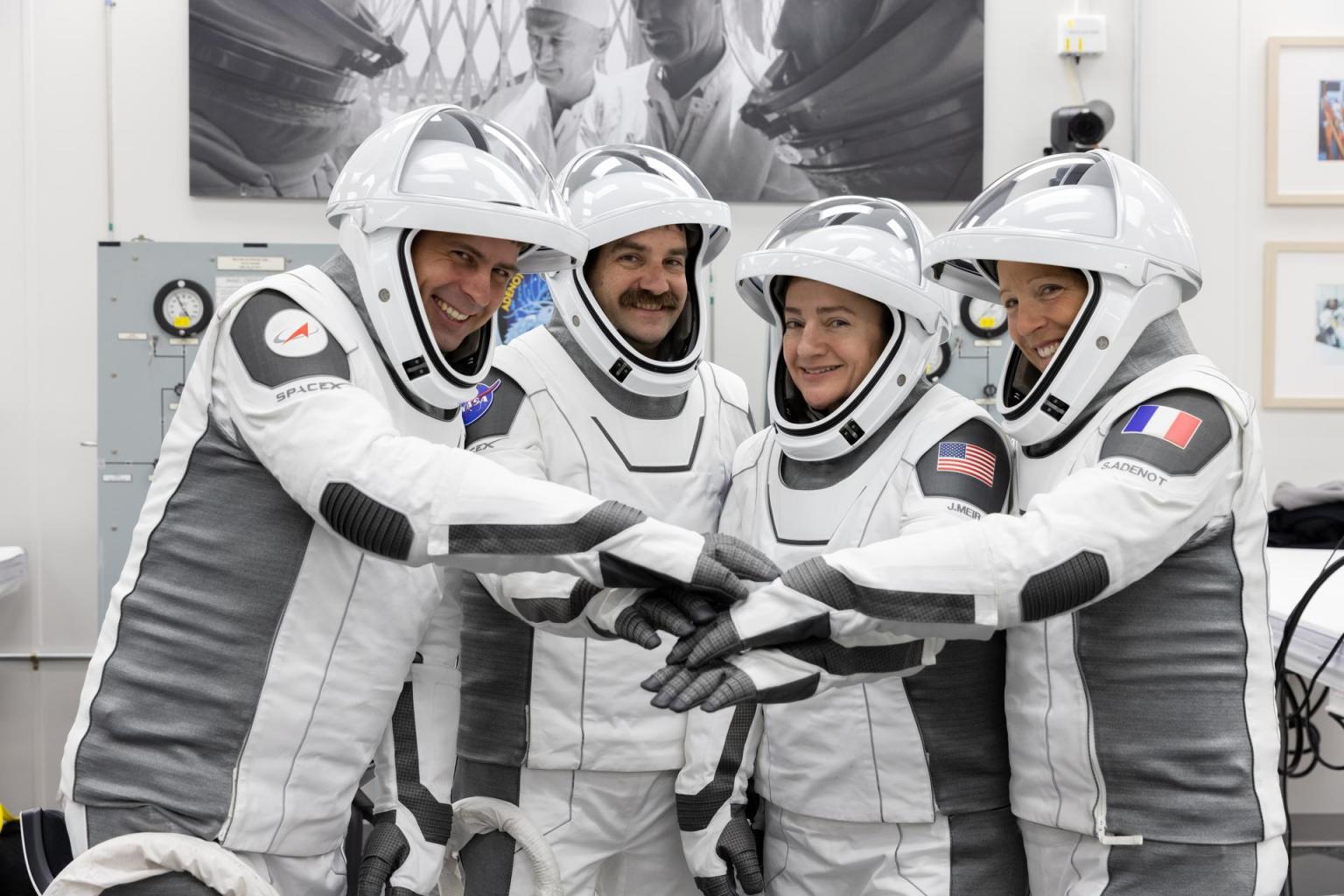 NASA's SpaceX Crew-12 astronauts stand side by side in their spacesuits with face shields raised. They extend their arms forward, stacking their hands together in a team huddle while smiling. Pictured at the Neil A. Armstrong Operations and Checkout Building at Kennedy Space Center ahead of their Feb. 13, 2026 launch to the International Space Station, from left to right: Roscosmos cosmonaut Andrey Fedyaev, NASA astronauts Jack Hathaway and Jessica Meir, and ESA astronaut Sophie Adenot.