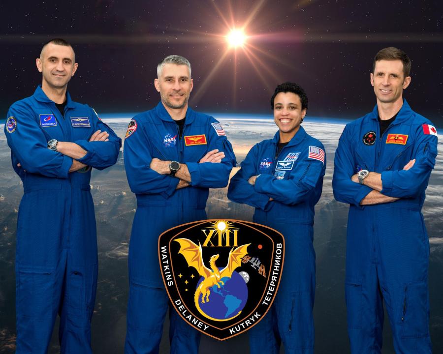 The four members of NASA’s SpaceX Crew-13 mission to the International Space Station stand in front of a decorative space background wearing blue flight suits.