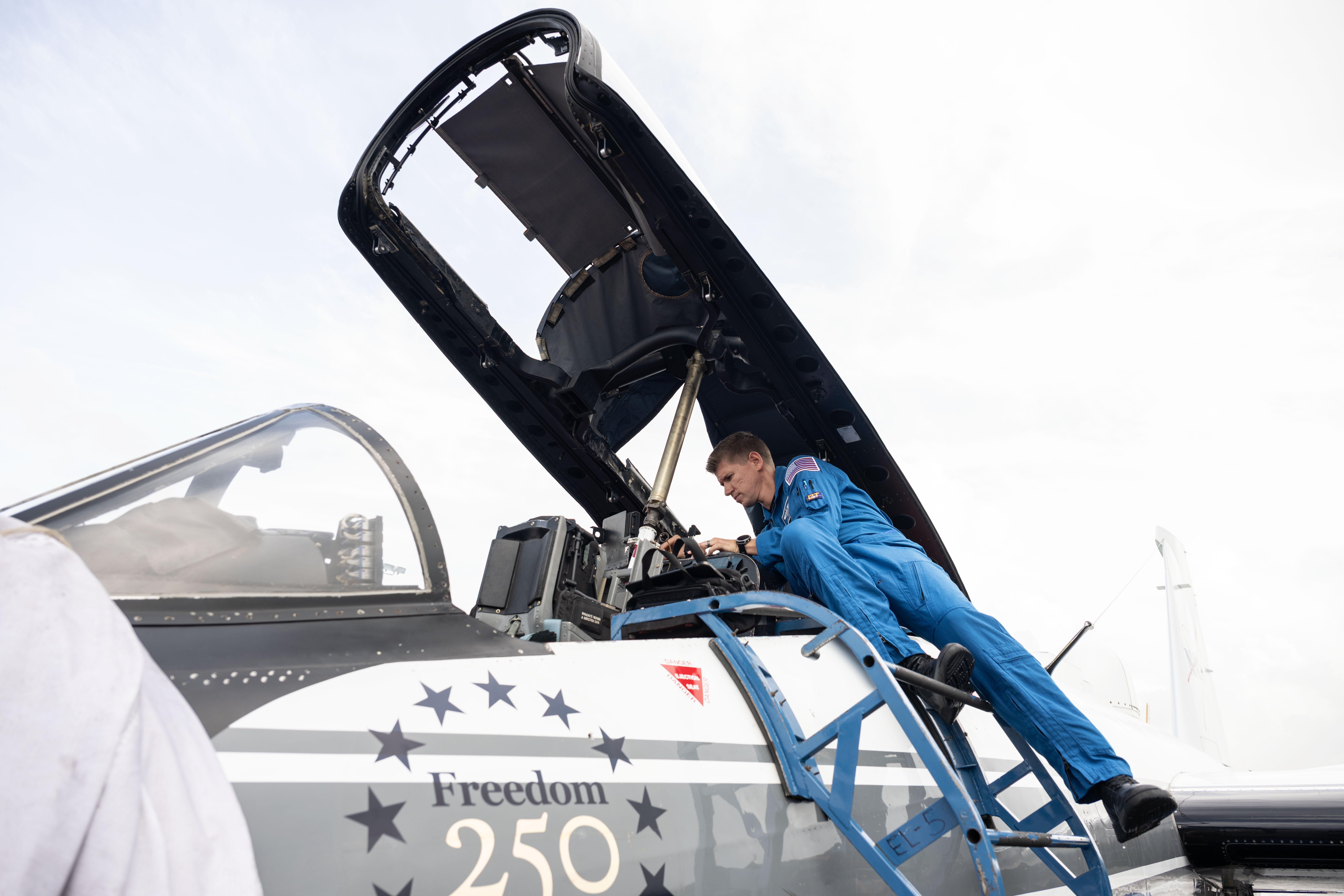 A man in a blue flight suits inspects the cockpit of a WB-57 aircraft.