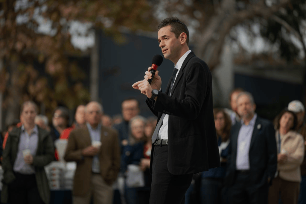 NASA's Administrator, Jared Isaacman, talking to a crowd outdoors while holding a microphone.