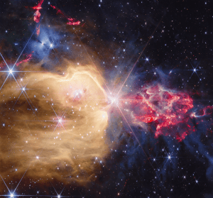 A young star cluster filled with many stars that display Webb’s unique eight-pronged diffraction pattern. At its center is a yellow star which sports the largest diffraction pattern. To the left of the star, there is a region filled with yellow dust and gas that extends from the star to the left border of the image. This yellow region extends from the bottom, covering about two-thirds of the image. The yellow region has several blue stars of different sizes embedded within. The top third, which lies outside of the yellow region, holds a few bright protostars, within dense gray gas. Those stars illuminate the gas, making it appear blue. A few red outflows from other protostars are visible above this grayish-blue region. To the right of the central star, there is a clumpy, flame-like plume of red dust and gas with protostars that emit a soft white light within. The plume is surrounded by more dense gray gas and dust. There are several background galaxies strewn throughout the image.