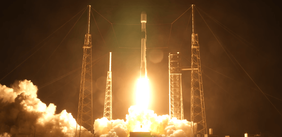 A SpaceX Falcon 9 rocket lifts off from its launch pad at in a dark sky, surrounded by an orange-white exhaust plume that illuminates billowing clouds of smoke.