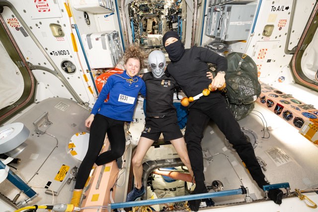 Three astronauts wearing costumes float in a space station module.