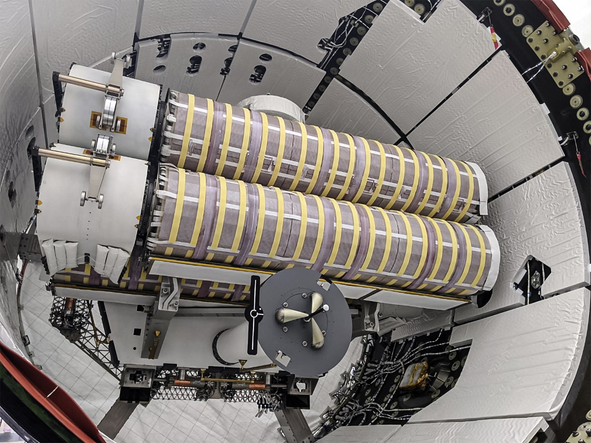 Two cylindrical Roll Out Solar Arrays wrapped in striped insulation are secured in the trunk of a SpaceX Dragon Cargo vehicle surrounded by structural supports and cables.