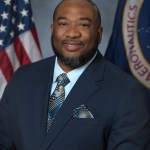 A studio portrait of Carl Sandifer wearing a navy blue suit and patterned tie.