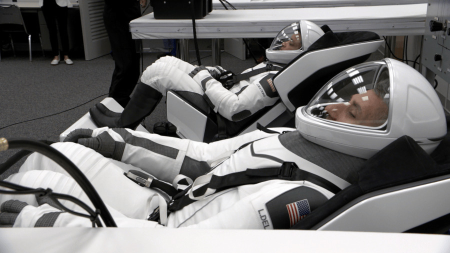 Astronauts in white spacesuits lying down during suit checks.