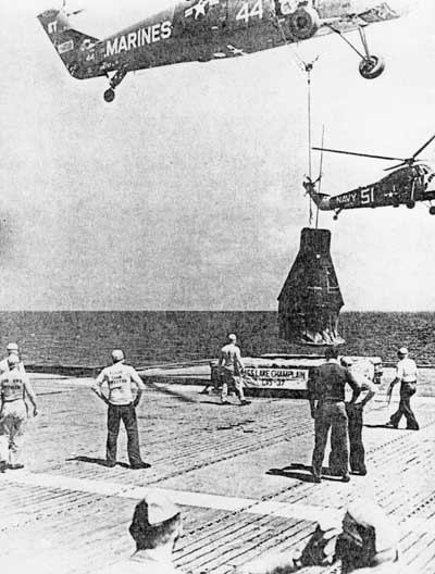 helicopter lowering recovered spacecraft onto carrier deck