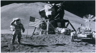 Photo of the Apollo fifteen landing site showing Irwin saluting the flag. The lander and rover are in the background.