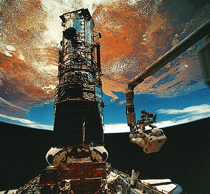 Photo of astronauts servicing the Hubble in the shuttle bay with the Earth overhead.