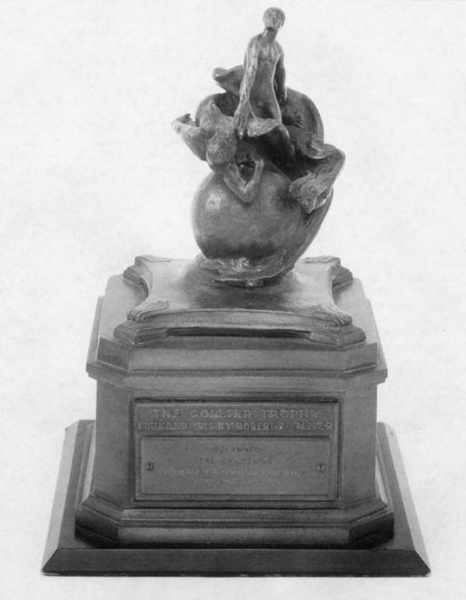 Photo of the Collier Trophy. Man astride the globe of the world holds a bird with outstreched wings in his right hand. Other wind spirits circle the globe.