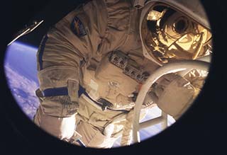 Close-up of Usachev outside of the Mir in his extravehicular mobility unit (EMU), waving to the camera.