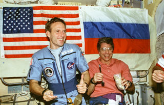 Mission Specialists Jerry Linenger and John Blaha at the table of Mir's Base Block sampling Russian food.