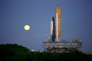 STS-86 Atlantis on crawler transport rolling out to the launch pad; full moon rises behind the shuttle