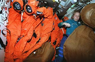 Mission specialist Marsha Ivins squeezes between a rack of launch and entry suits hung up in preparation for donning before re-entry. 