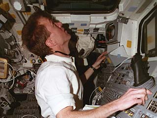 Photo documents STS-81 crew activities during the undocking with the Mir space station including: pilot Brent Jett working with the aft flight deck controls as he watches out of the overhead windows. 