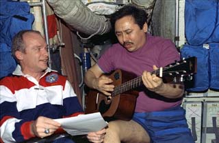Mir-25 commander Talgat Musabayev plays a guitar while STS-91 commander Charlie Precourt holds up sheet music. 