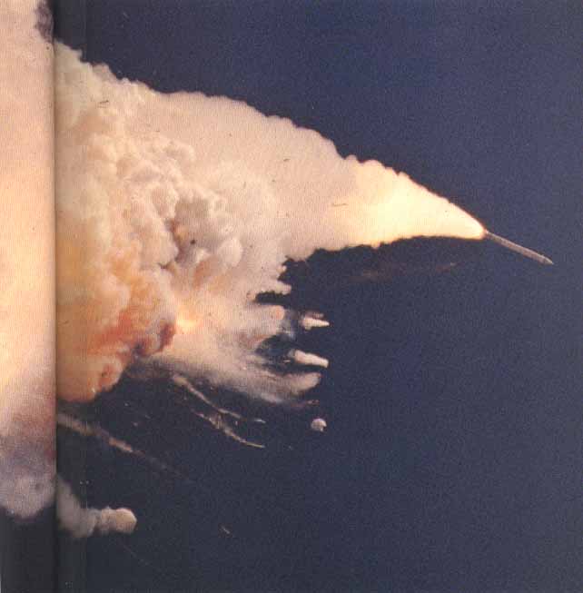In the photo at right, the left booster (far right) soars away, still thrusting. The reddish-brown cloud envelops the disintegrating Orbiter. The color is characteristic of the nitrogen tetroxide oxidizer in the Orbiter Reaction Control System propellant.